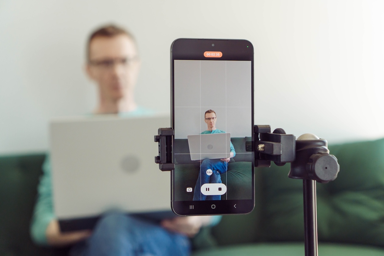 Man sitting on a couch filming a video with a smartphone camera