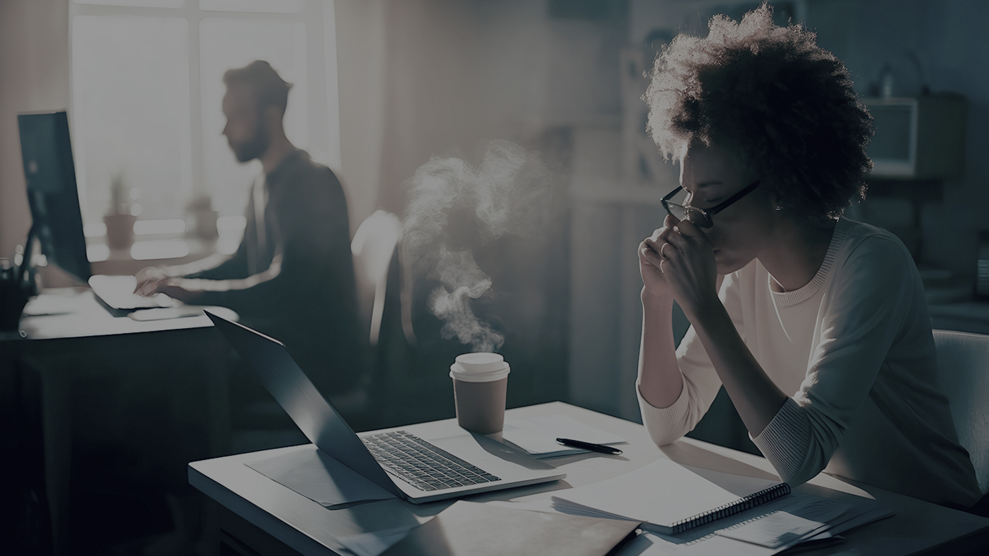 Focused woman working at a desk with documents, laptop and coffee in soft morning light.
