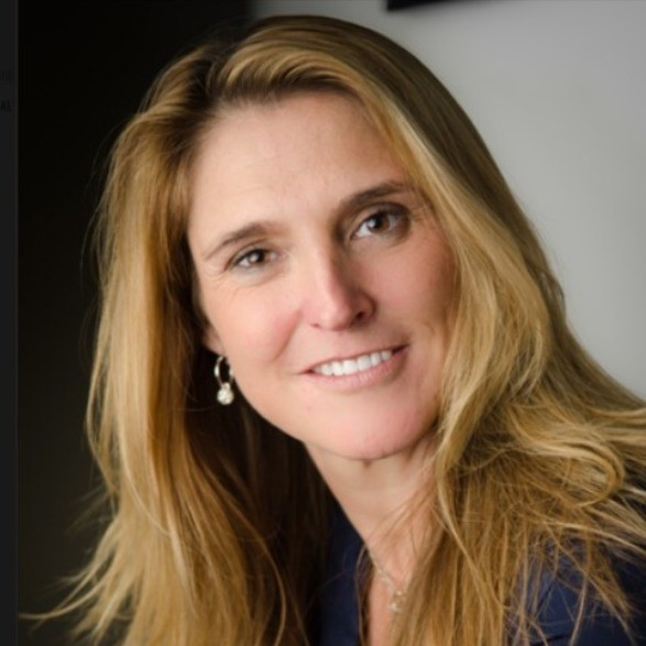 Portrait of a smiling woman with long blonde hair and pearl earrings against a dark and light background.