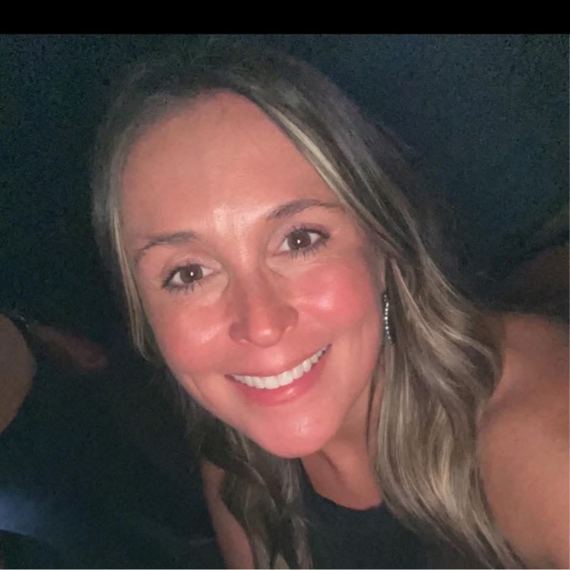 Close-up of a smiling woman with long blonde hair in a dark setting.