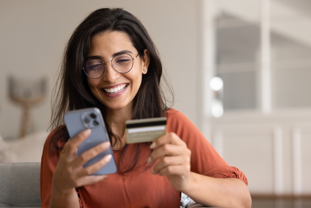 Mujer usando su celular y una tarjeta de débito para realizar una recarga telefónica
