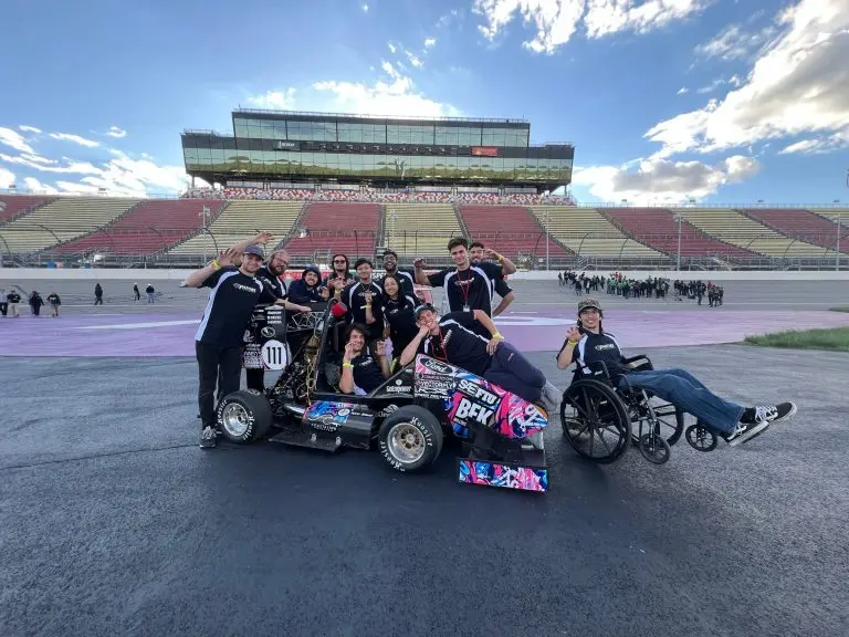 SAE FIU student racing team gathered with their competition car at the racetrack