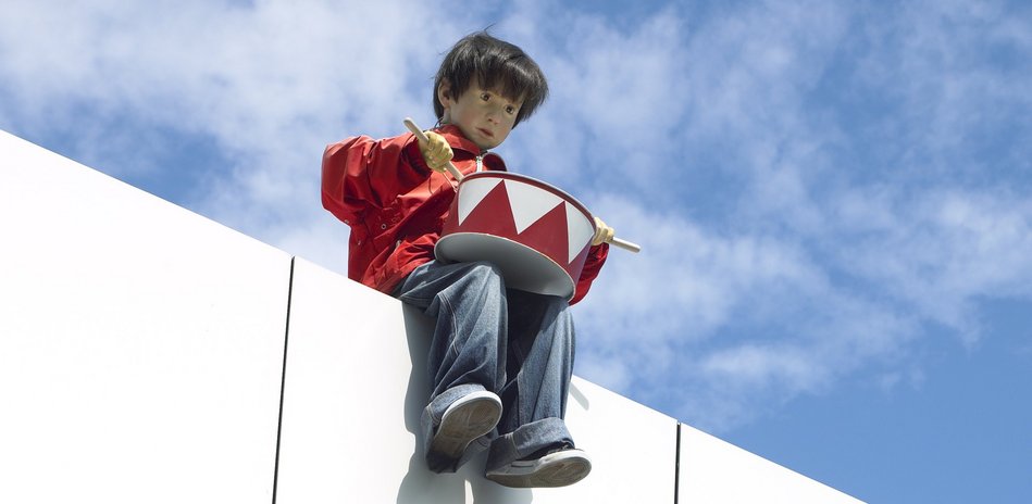 Maurizio Cattelan, Untitled, 2003, a childlike drummer figure sitting high on a ledge.