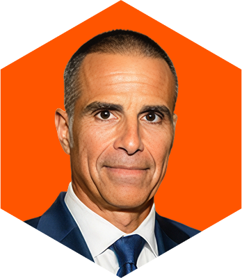 Portrait of a middle-aged man with short dark hair, wearing a navy blue suit, white shirt, and blue tie against an orange hexagonal background.