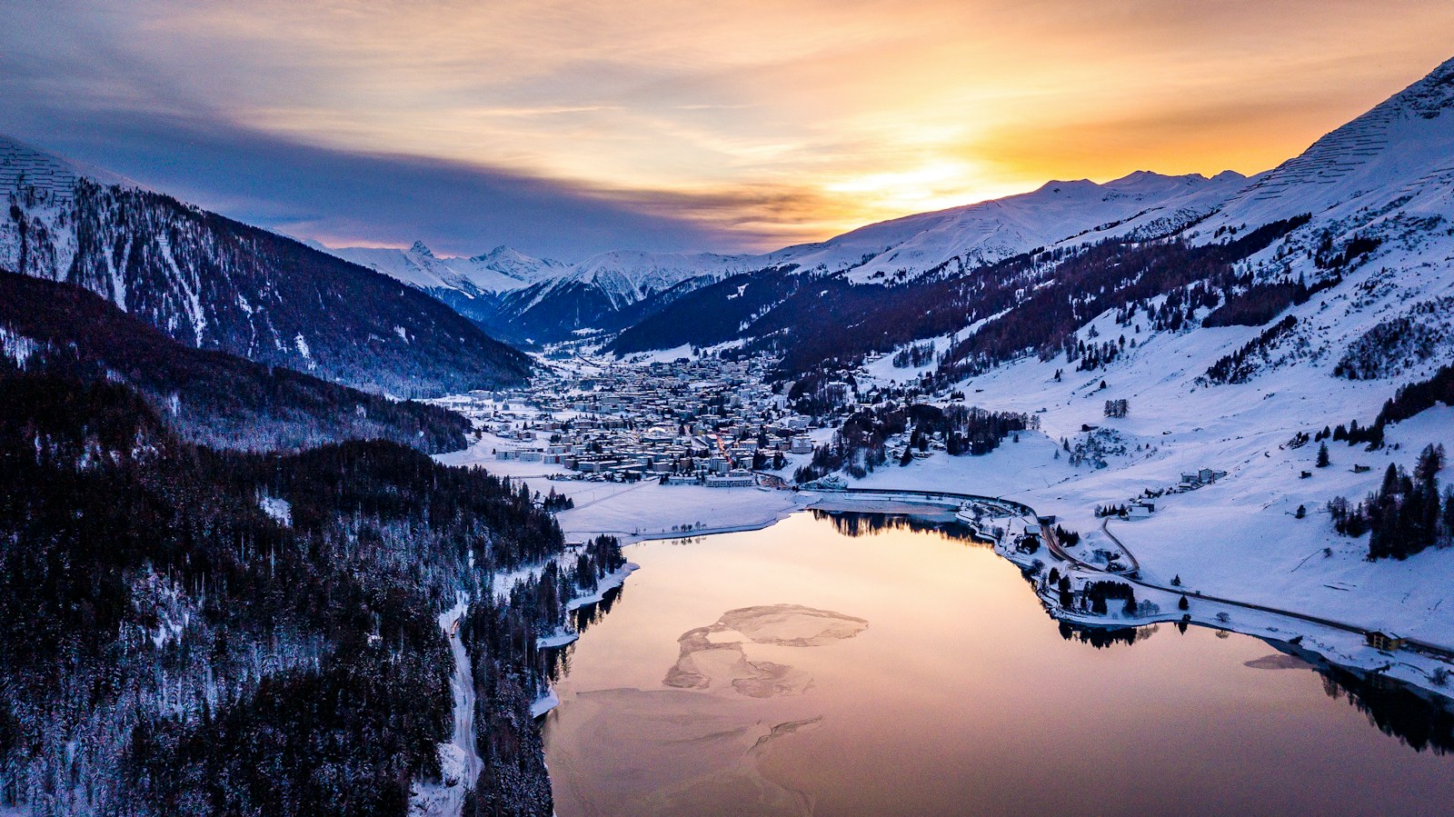 Snow-covered Davos and Lake Davos surrounded by mountains at sunset. Photo by Damian Markutt on Unsplash.