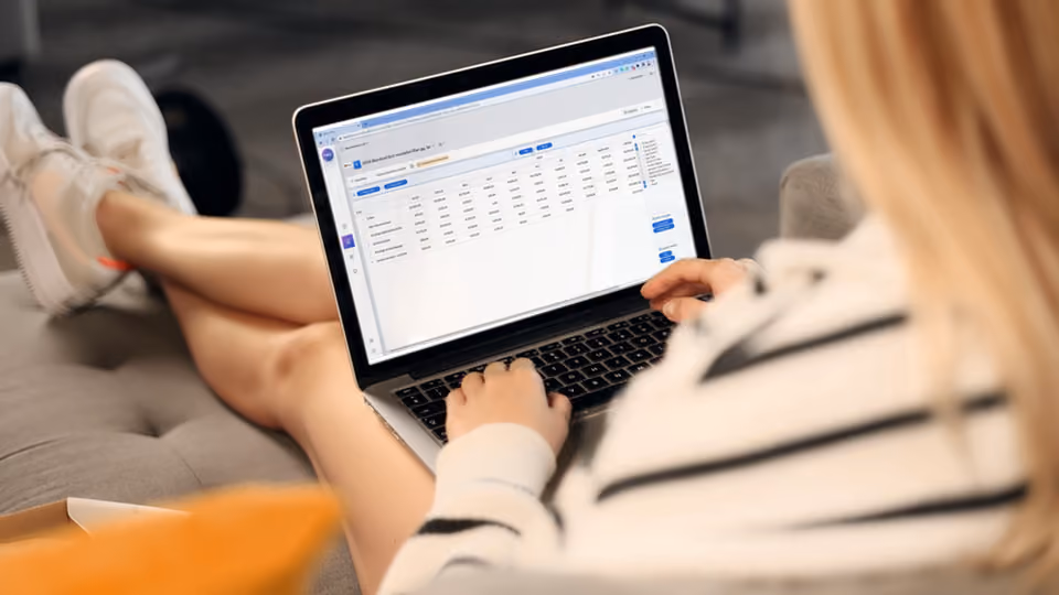 Person in a striped shirt working on a laptop displaying a spreadsheet or data table.