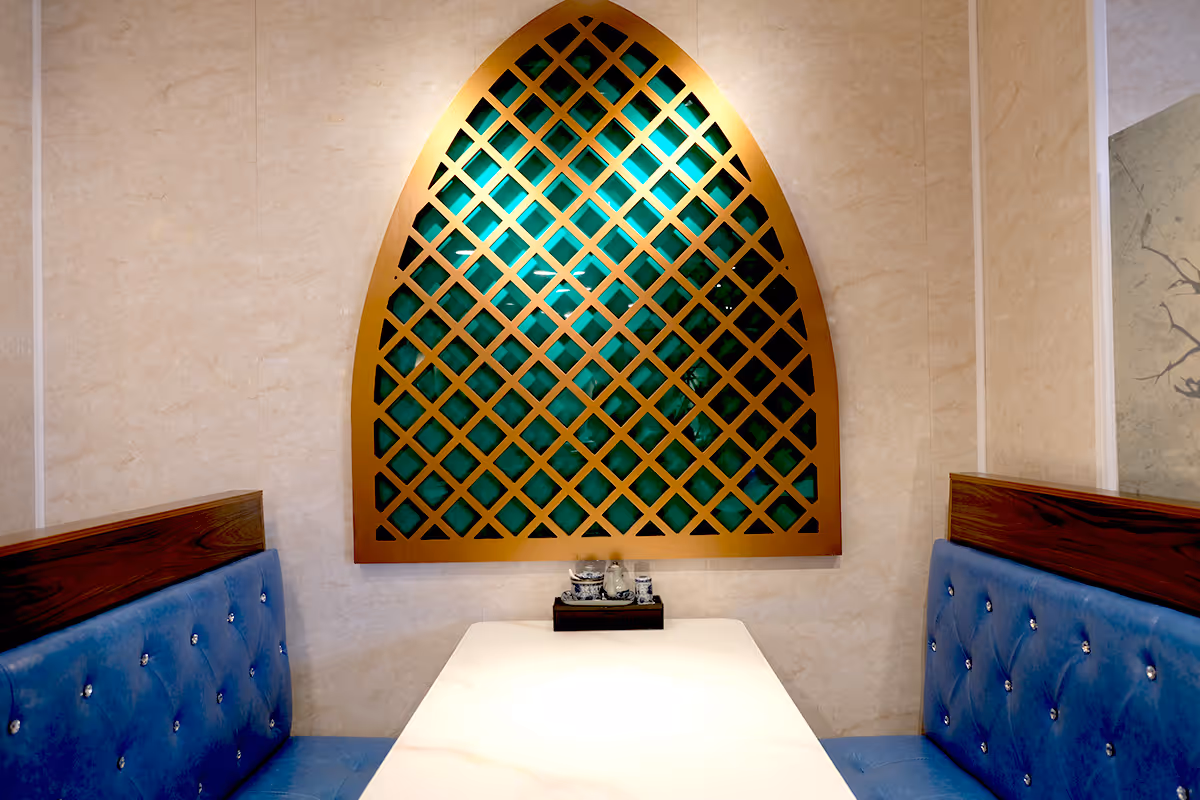 Interior photographs of Joo Chiat Branch. Cosy dining nook with blue cushioned bench seating on both sides and a white table, featuring a decorative arched lattice wall panel with green backing.