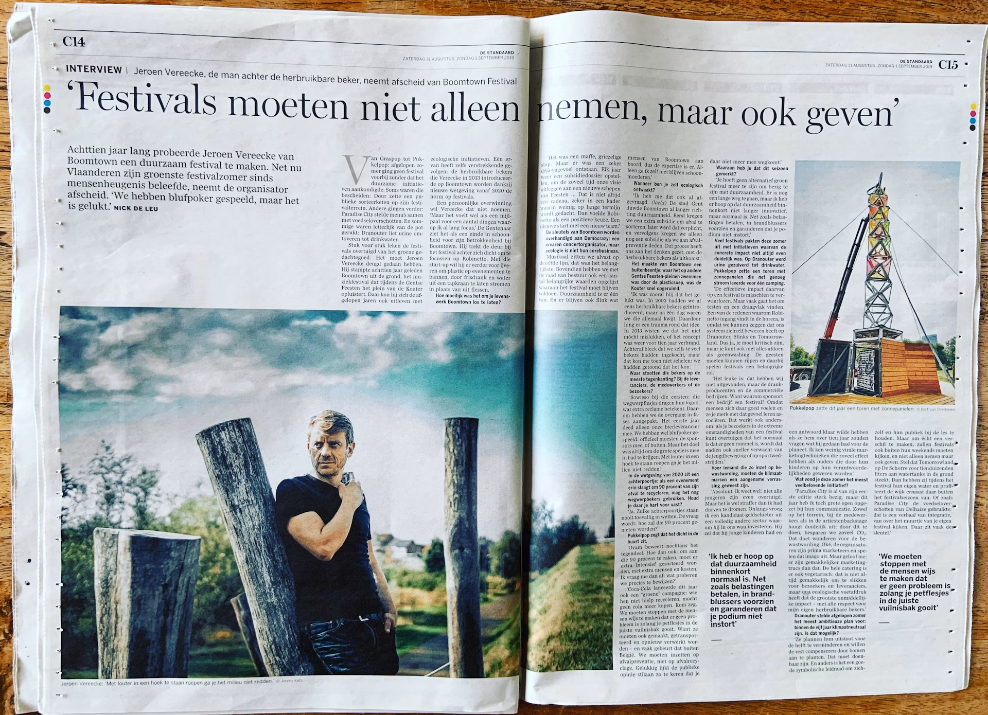 Een opengevouwen krant met een interview over duurzame festivals. Links een grote foto van Jeroen Vereecke, oprichter van Robinetto, bij houten palen in een groen landschap. Rechts een kleinere afbeelding van een torenconstructie.