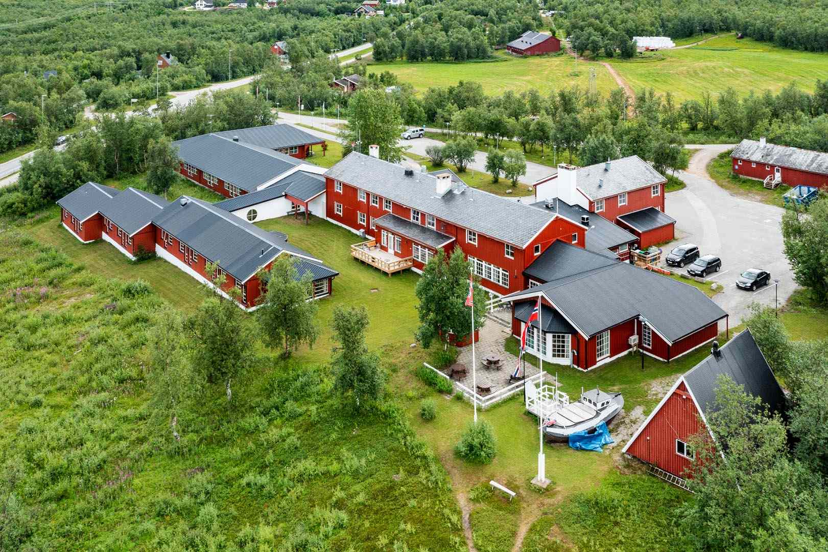 Oversiktsbilde av hele Lakselv Hotell-anlegget sett fra luften, med røde bygninger og grønne omgivelser.