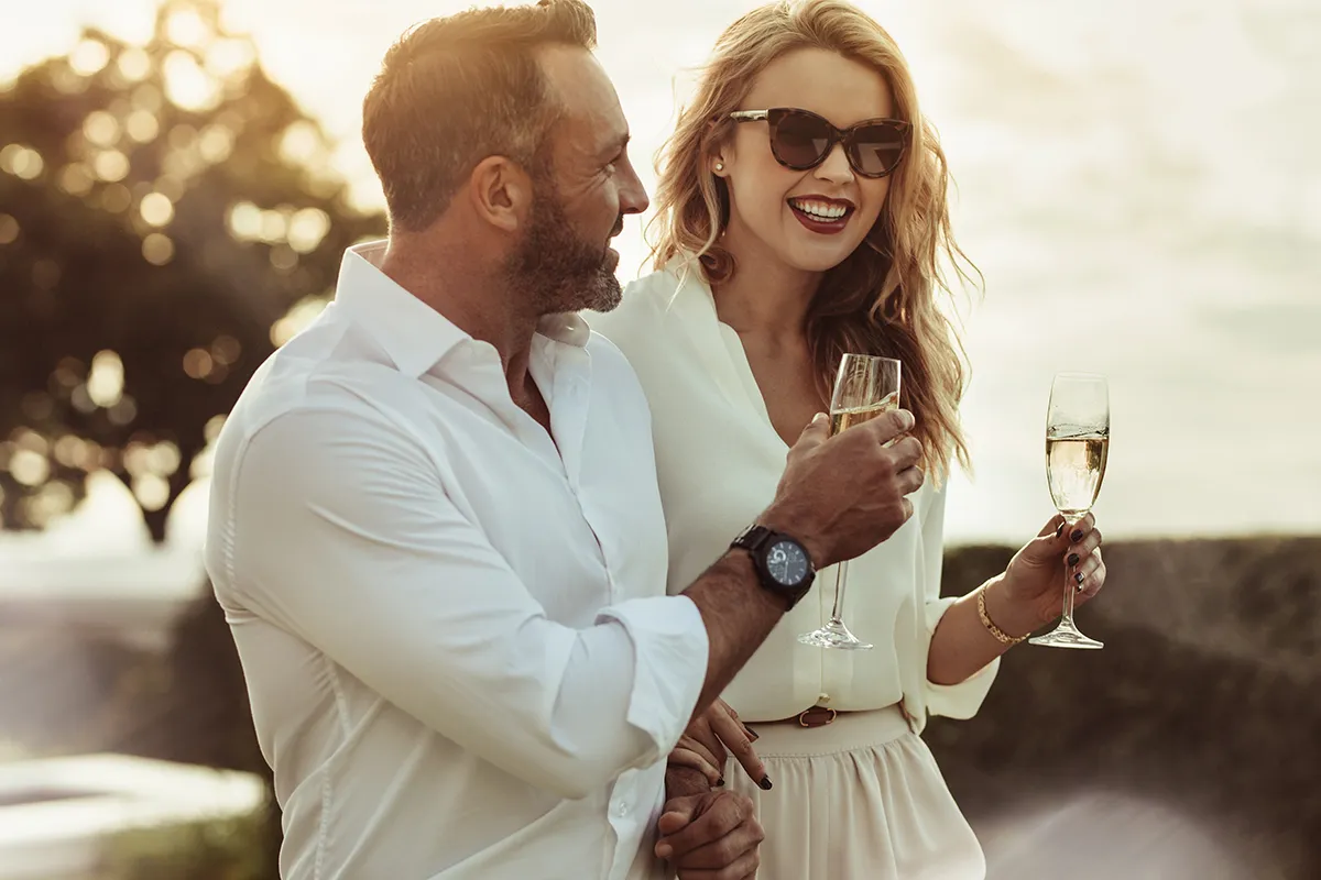 Two smiling adults holding stemmed glasses outdoors.