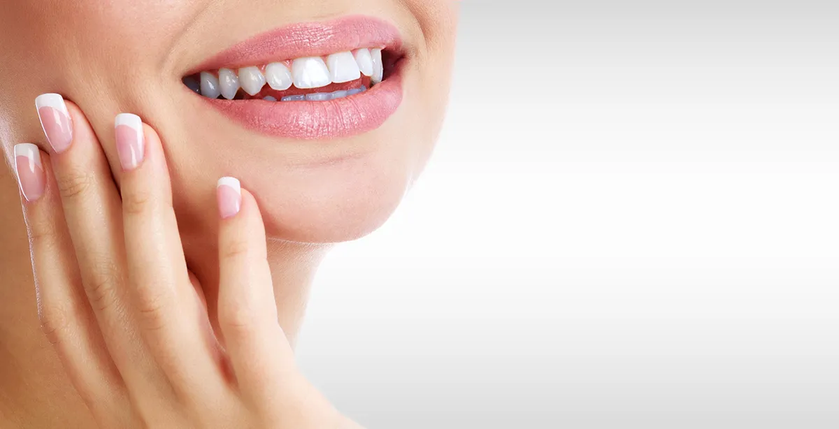 Close-up of a smile with a hand resting against the cheek.