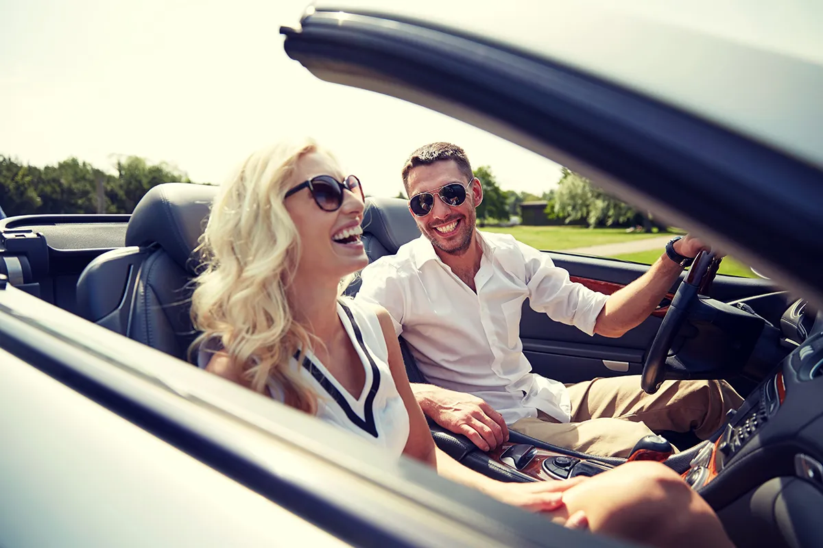 Two smiling adults sitting in a convertible car.