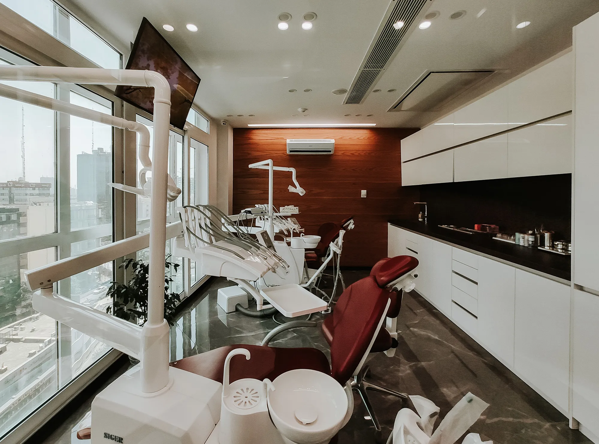 Dental treatment room with chairs beside tall windows.