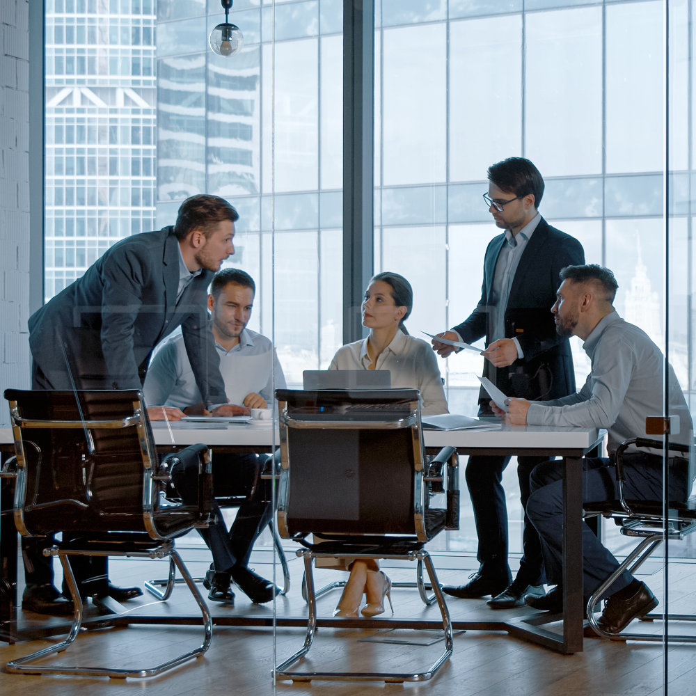 Une équipe d'hommes et une femme en réunion d'affaires dans une salle de conférence avec de grandes fenêtres donnant sur la ville.