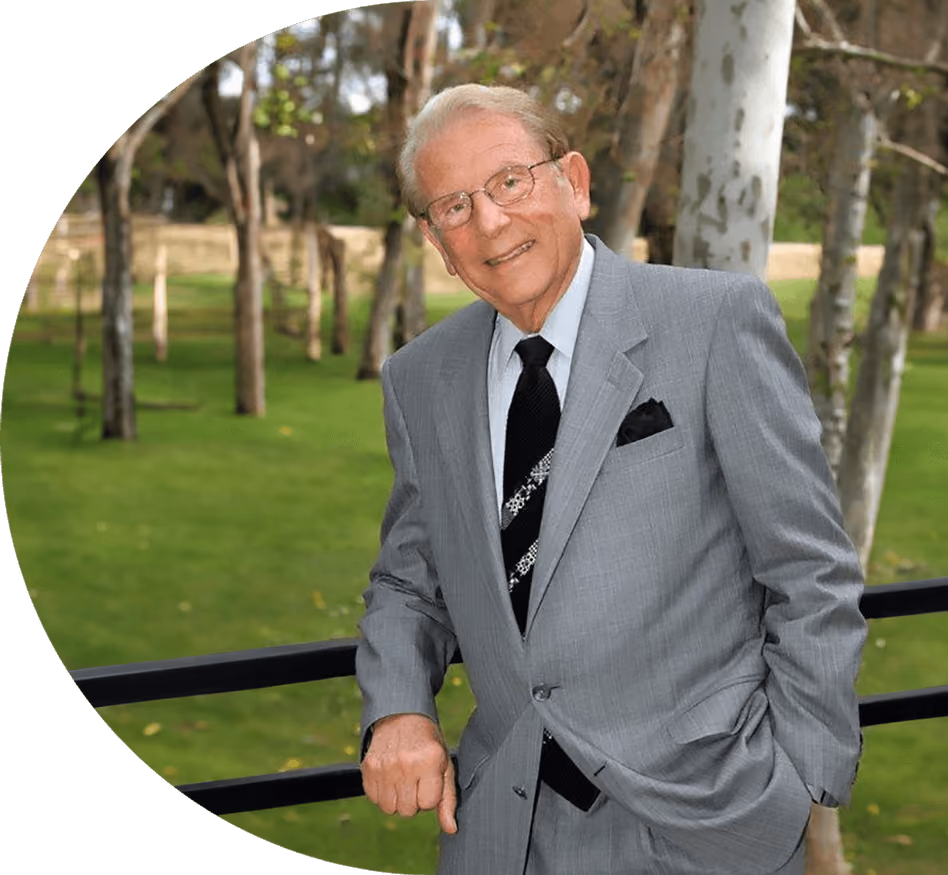 a man in a suit and tie standing in front of trees