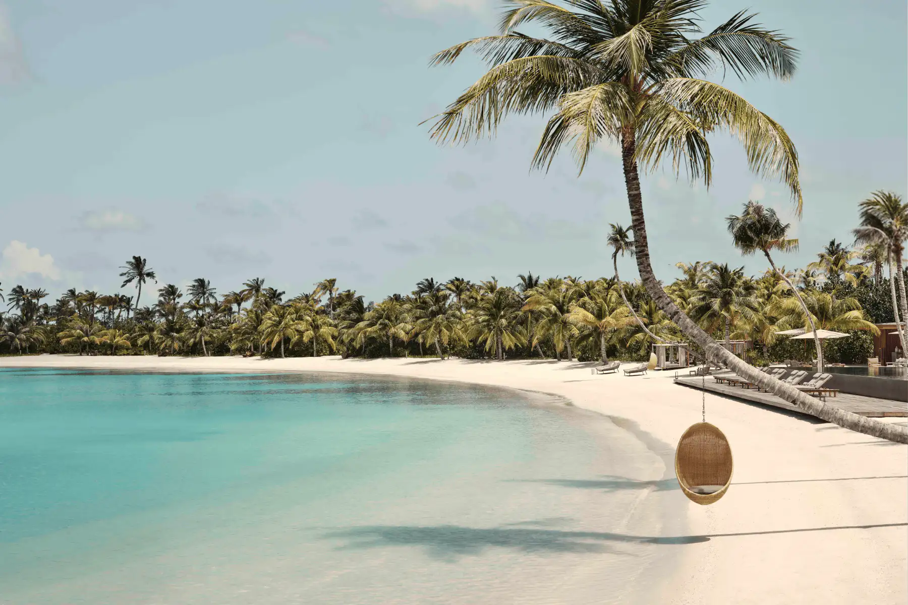 Calm turquoise ocean waves gently lapping a sandy beach bordered by large boulders and green tropical vegetation.