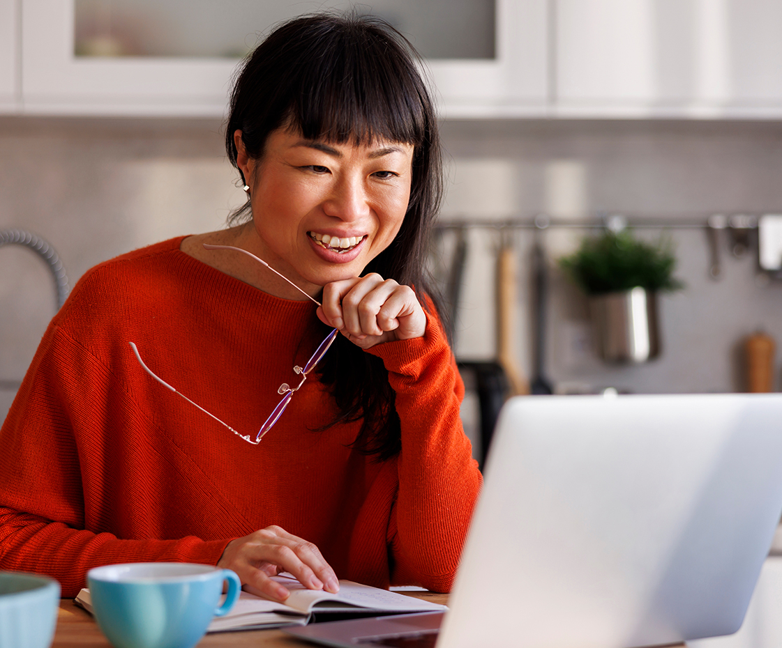 A strata owner in a red jumper working at a laptop at home.