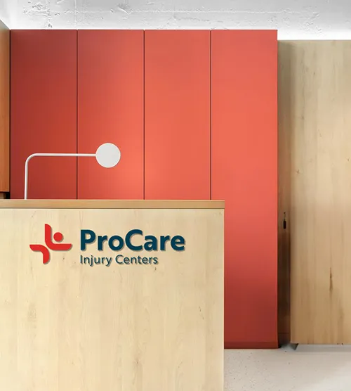 Reception desk with 'ProCare Injury Centers' logo, light wood panel and red vertical panels in background.
