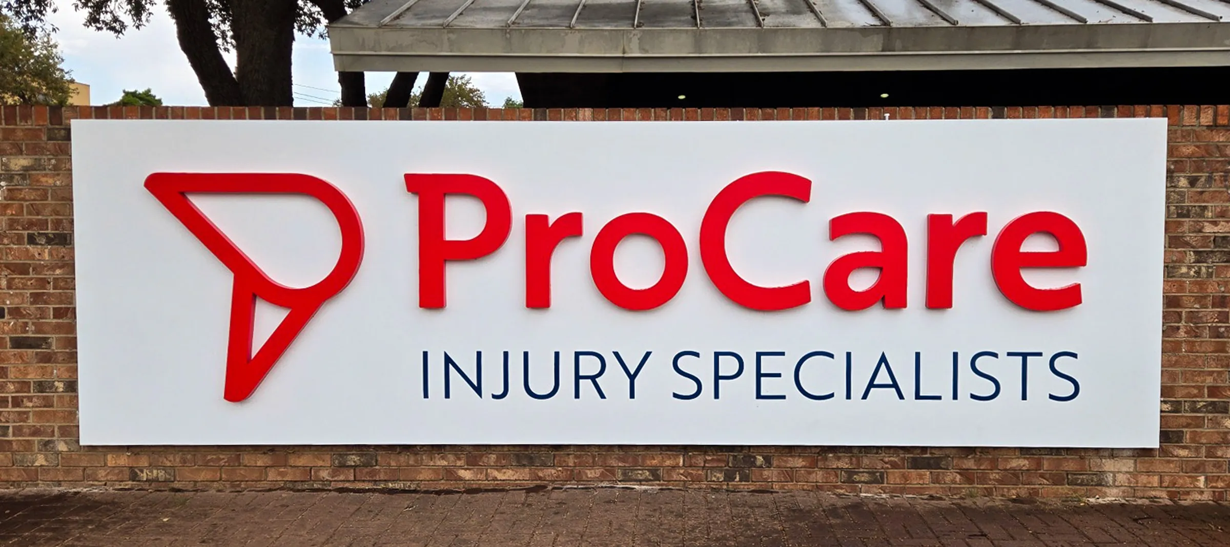 Sign on brick wall displaying 'ProCare' in large red letters with 'Injury Specialists' underneath in smaller blue letters.