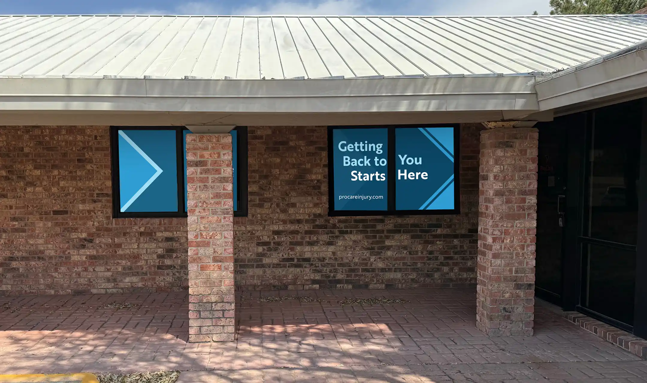 Brick building exterior with three windows, two displaying blue arrows and a message reading 'Getting Back to Starts You Here' with procareinjury.com.