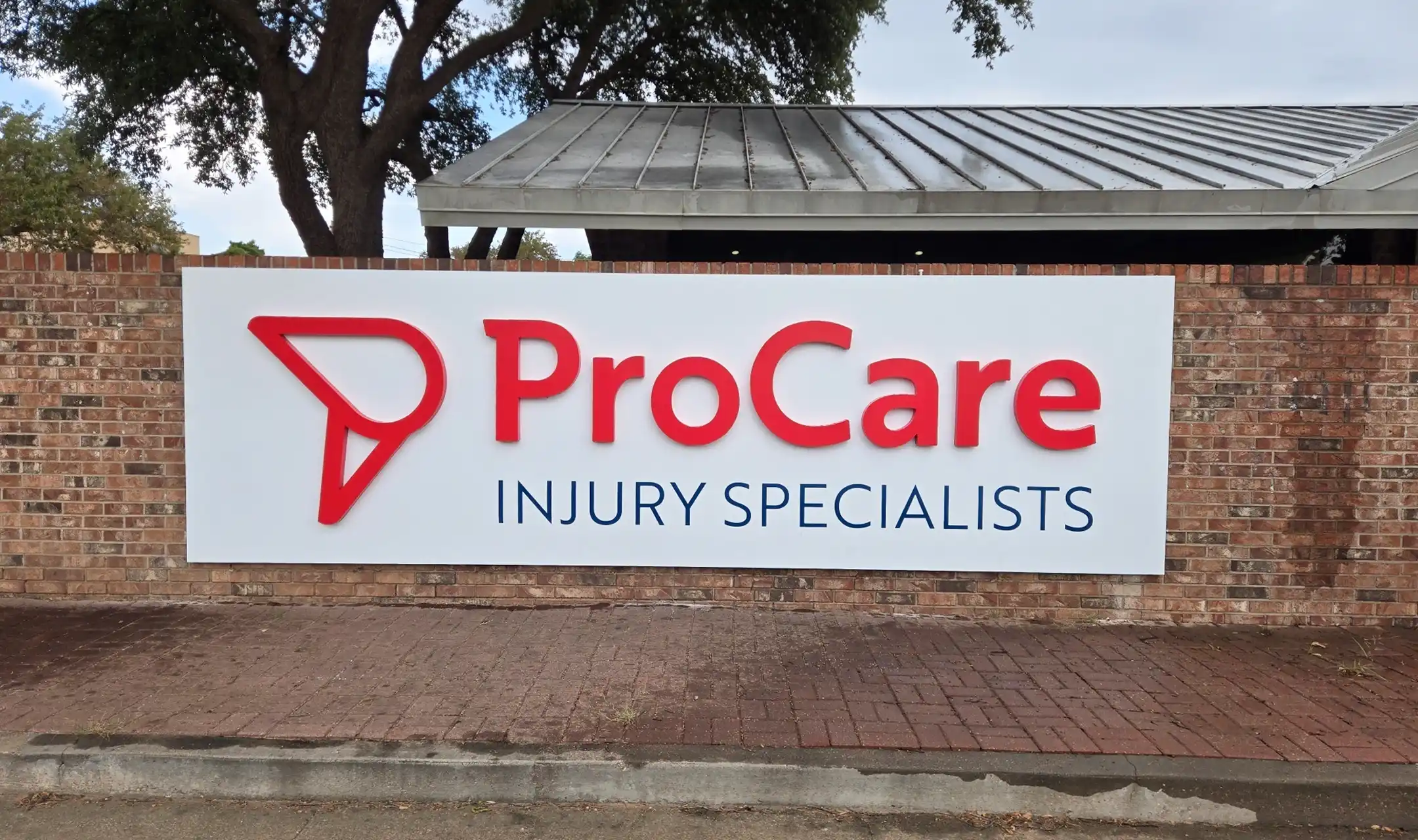 Outdoor sign on a brick wall with red logo and text reading 'ProCare Injury Specialists'.