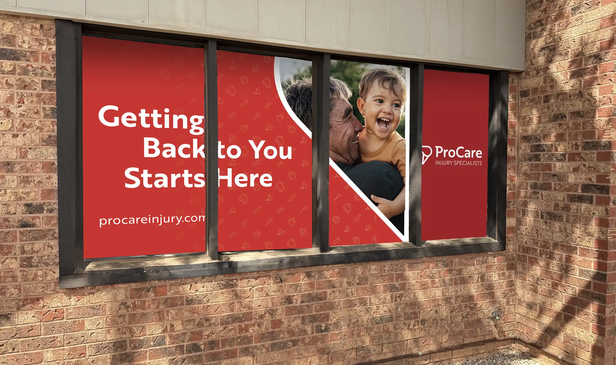 Window display with red background, text 'Getting Back to You Starts Here', ProCare Injury Specialists logo, and image of a man holding a laughing toddler.