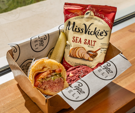 A catering box with a sandwich, pickle, chips and a cookie