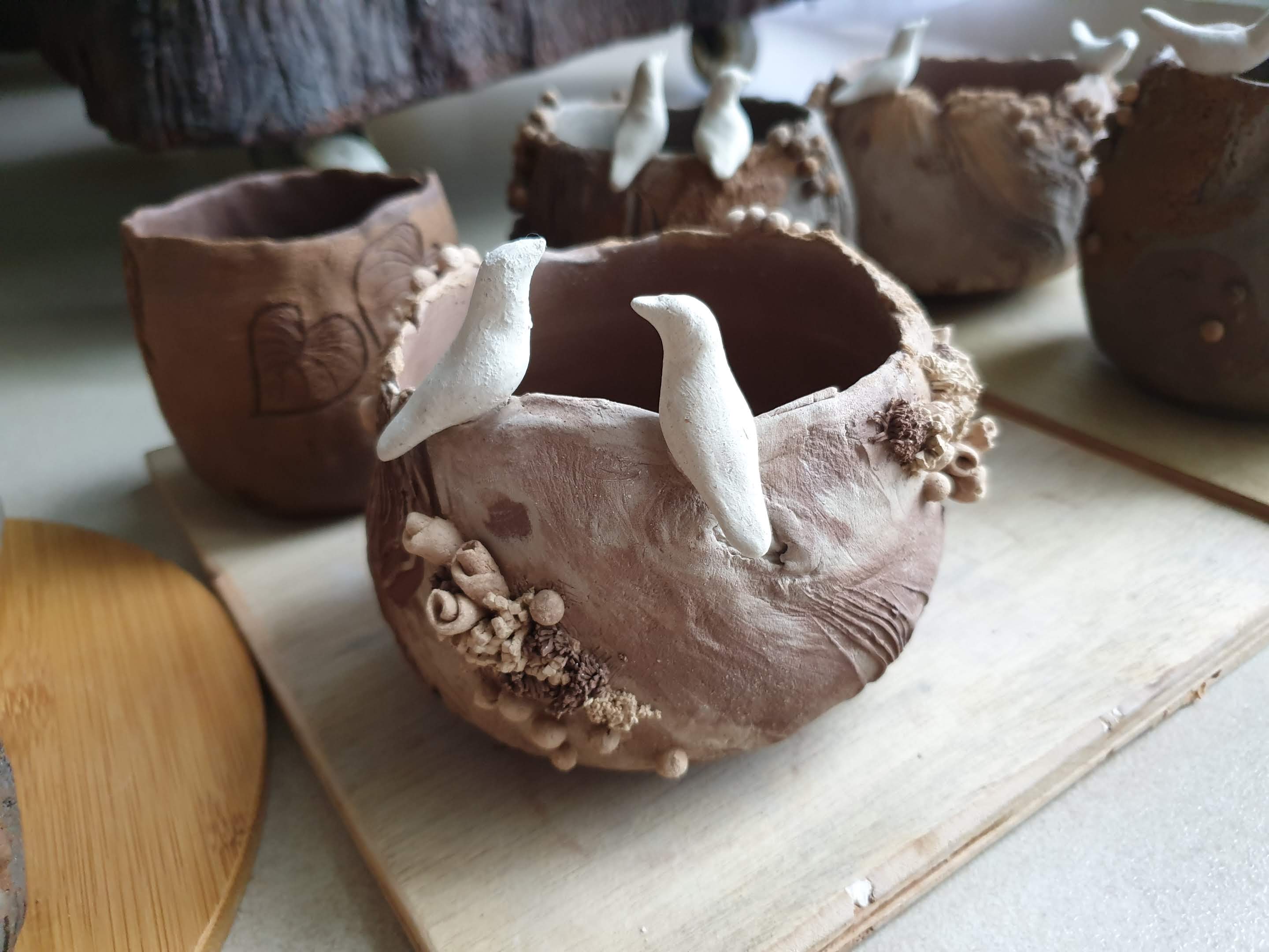 A photo of some stoneware plant pots I made. They have little white birds perched on the rim, and are still at greenware stage waiting to dry before they can be fired in a kiln.