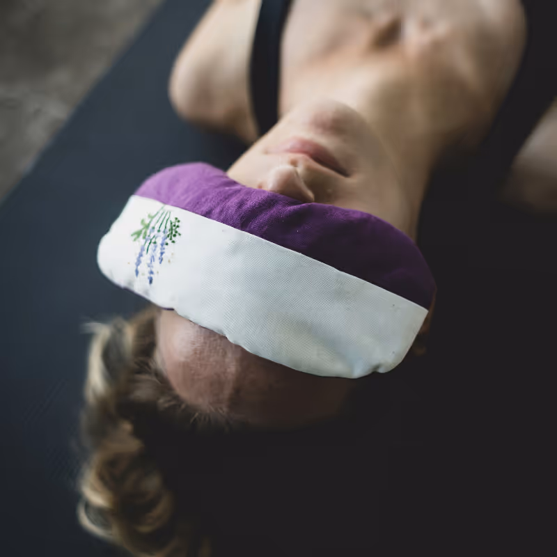 A close-up of a person lying down in savasana with a lavender eye pillow, signaling deep relaxation and nervous system regulation