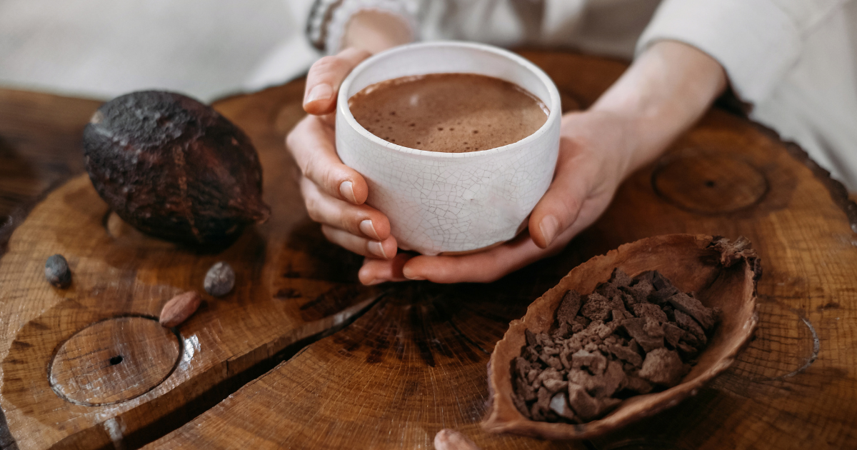 Hand holding a rustic ceramic mug filled with a steaming adaptogenic cacao latte—capturing a calming hormone-balancing ritual.