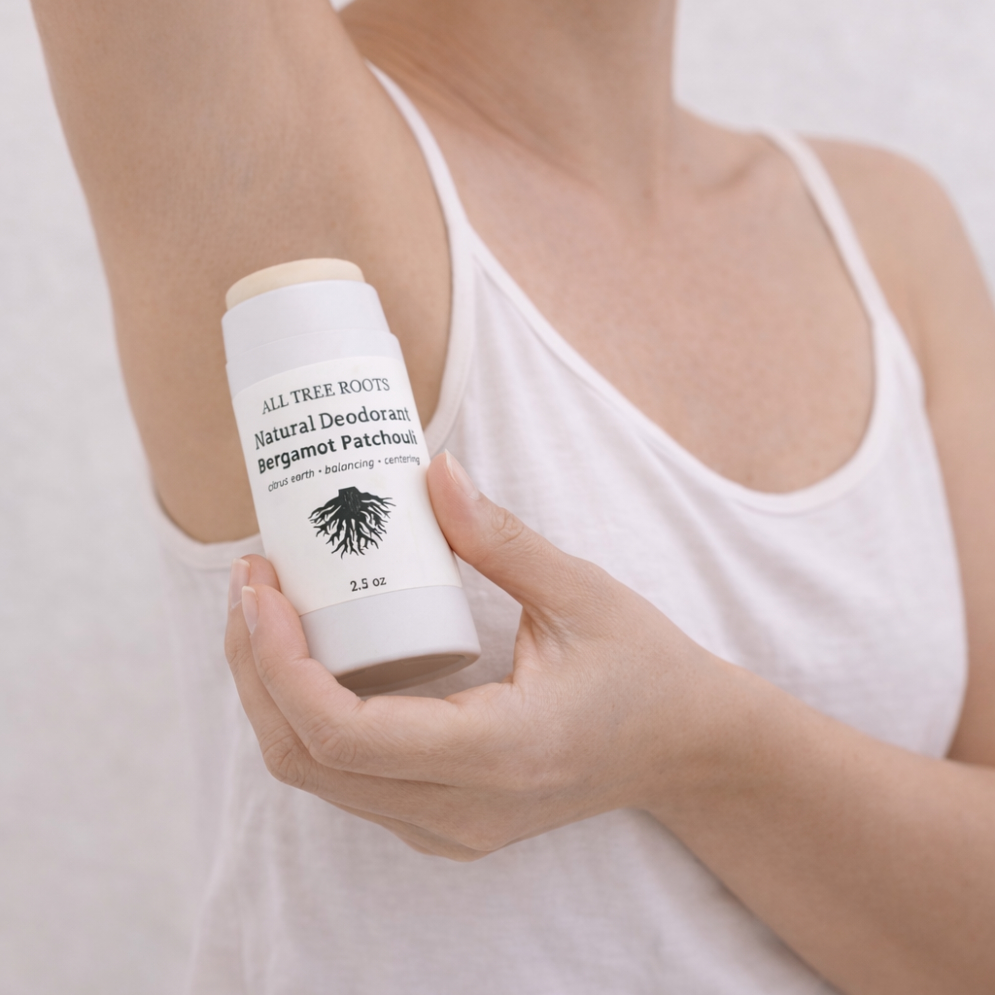 Person applying All Tree Roots Bergamot Patchouli deodorant.Person applying All Tree Roots natural deodorant from a paper push-up tube in soft, natural light.