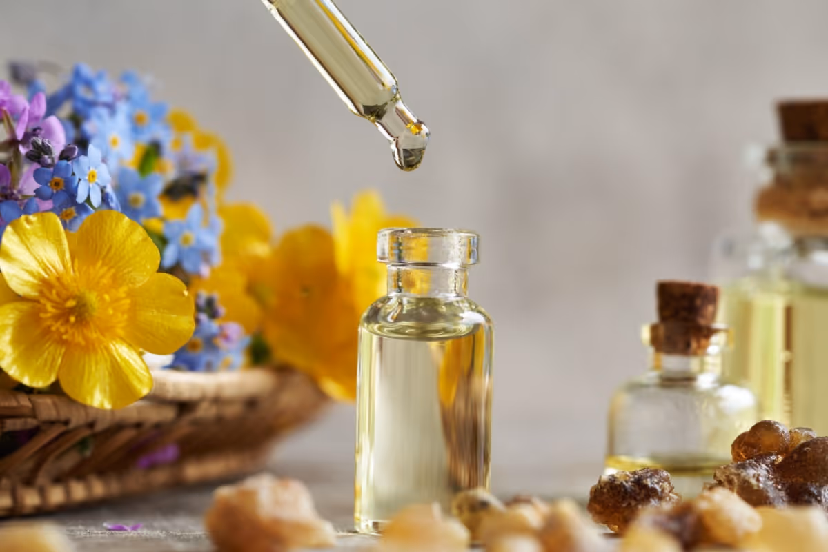 Glass bottle of essential oil surrounded by botanical flowers on a neutral background.