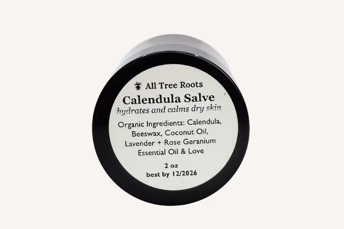 mber glass jar All Tree Roots Calendulal salve with a simple label showing essential oils used on a neutral background.