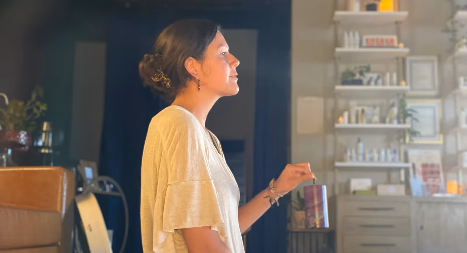 Sound healing facilitator speaking to participants while holding a chime in a softly lit wellness studio.