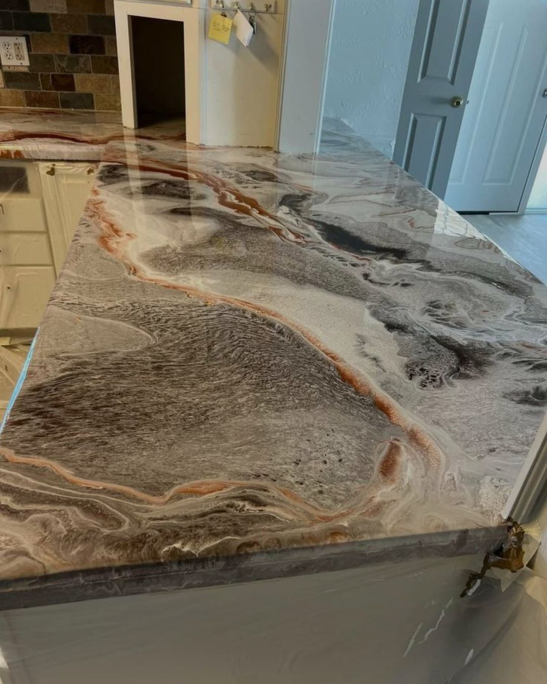 Glossy kitchen countertop finished with a custom marble-effect epoxy coating in gray, white, brown, and copper tones.