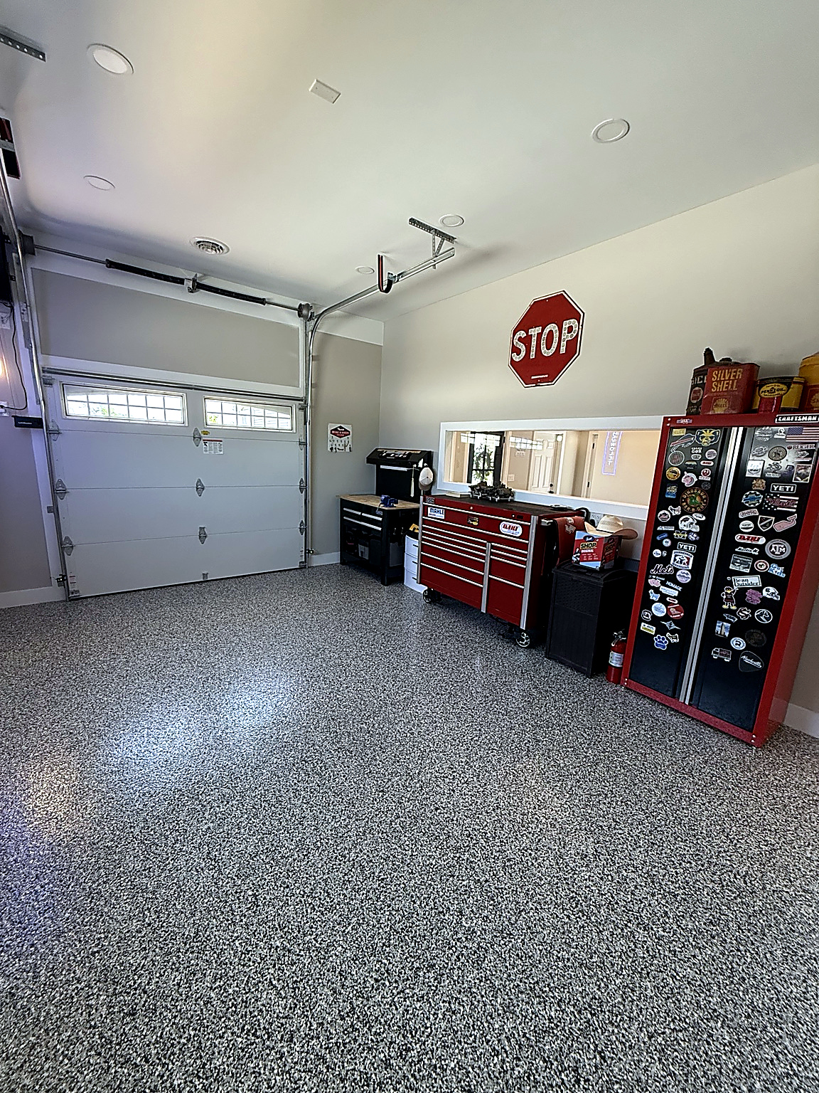 Modern garage with a glossy gray epoxy floor, black storage cabinets, tire racks, warm lighting, and a classic black car.