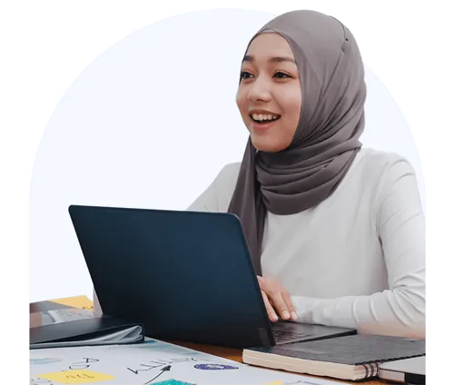 A woman sits at a table in front of a laptop smiling