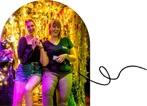 Two Ting employees pose in a photo booth in front of a glimmering gold curtain