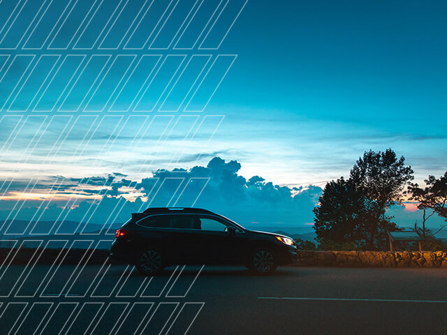 A Subaru drives in dusk with headlights on.