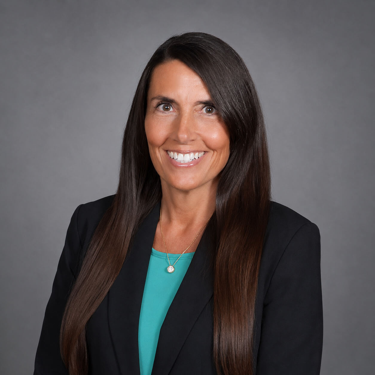 Sallie Reid, ACV's VP People & Culture, smiles at the camera in a dark teal shirt and black blazer.
