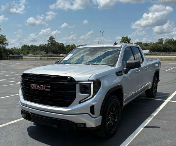 A white GMC Sierra on an unpaved parking lot
