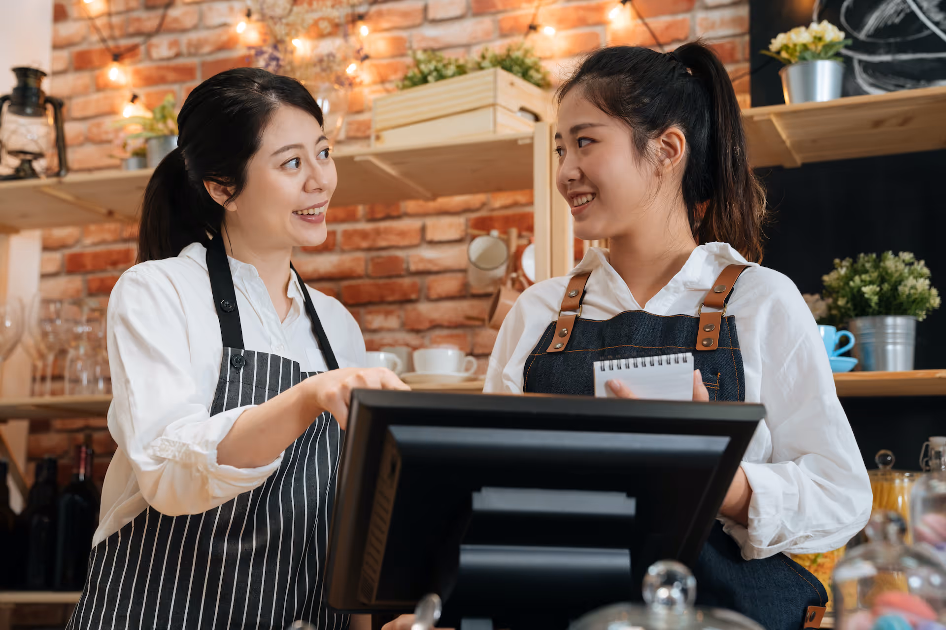 Two smiling female baristas working together behind bar counter