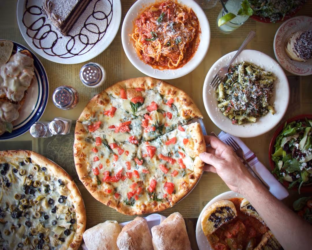 table spread with pizza, pastas, cakes, and a cocktail
