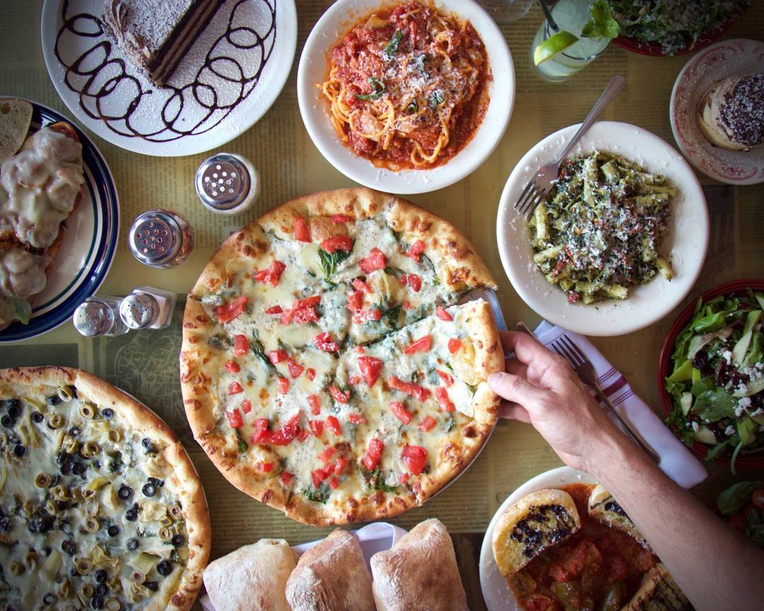 table spread with pizza, pastas, cakes, and a cocktail