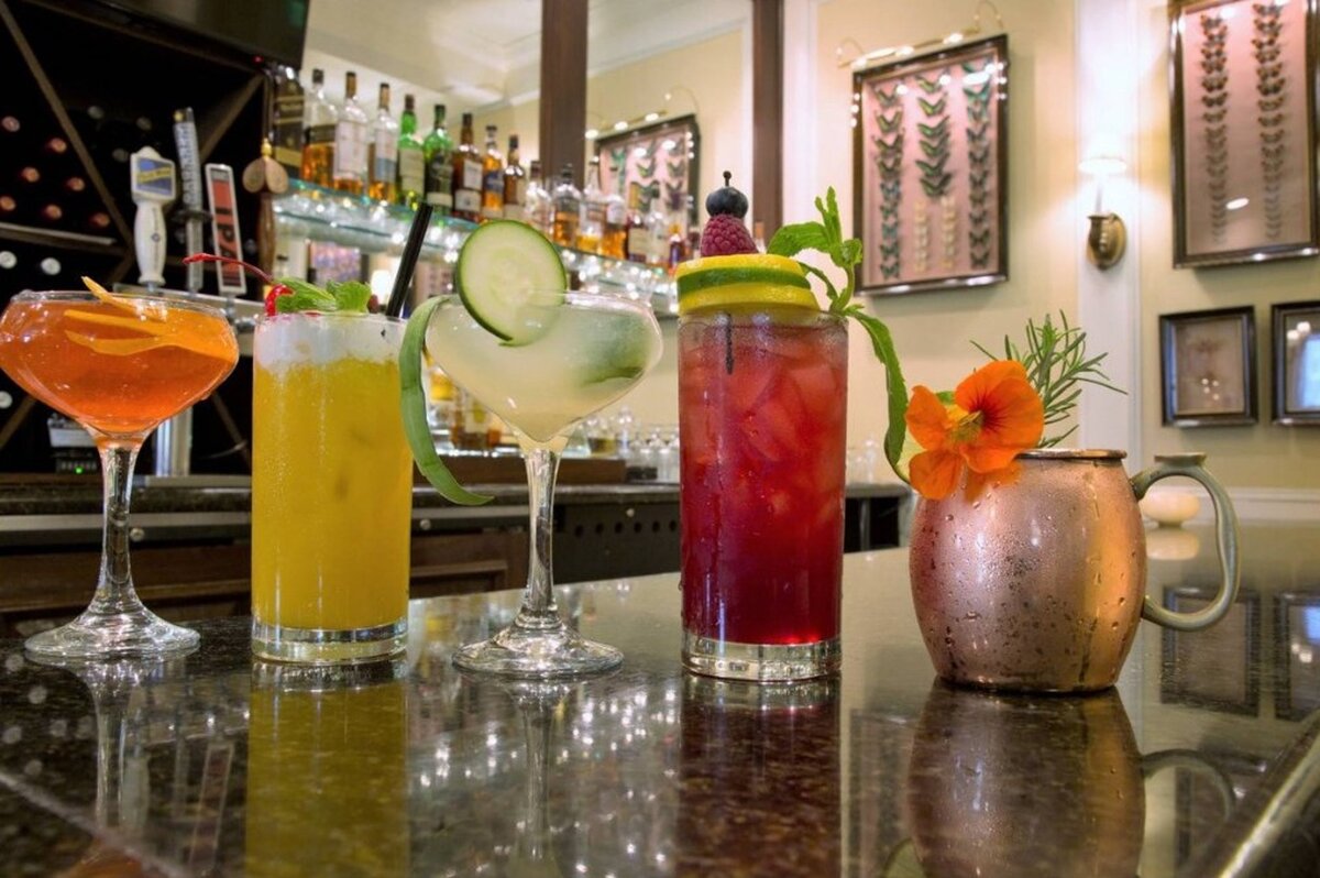 colorful cocktails lined up at on the counter of a fully-stocked bar