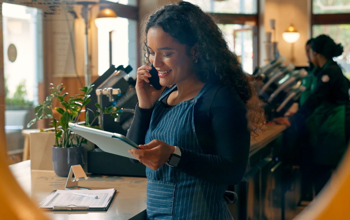 Restaurant employee speaking on the phone while checking information on a tablet