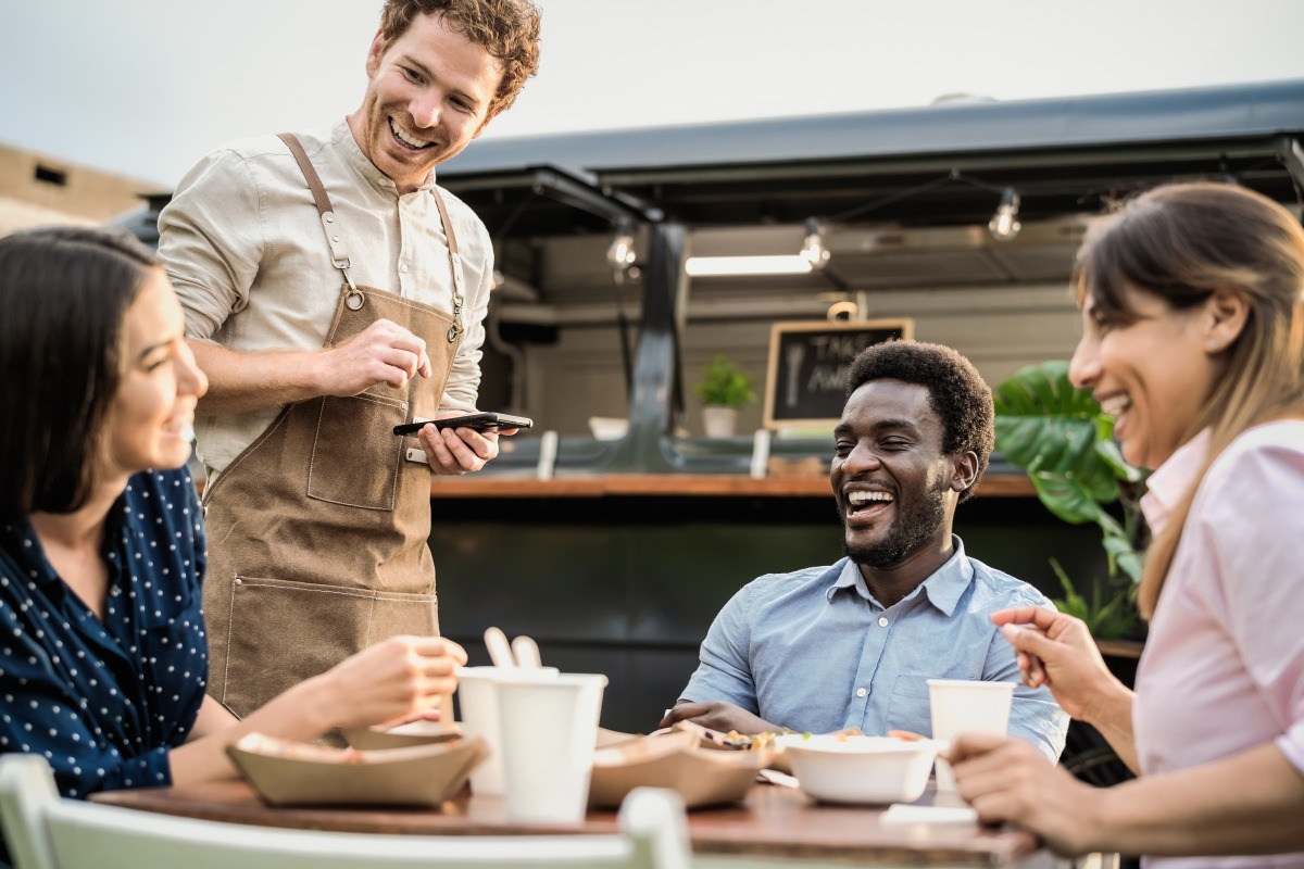 Server taking an order from three customers dining at an outdoor table.