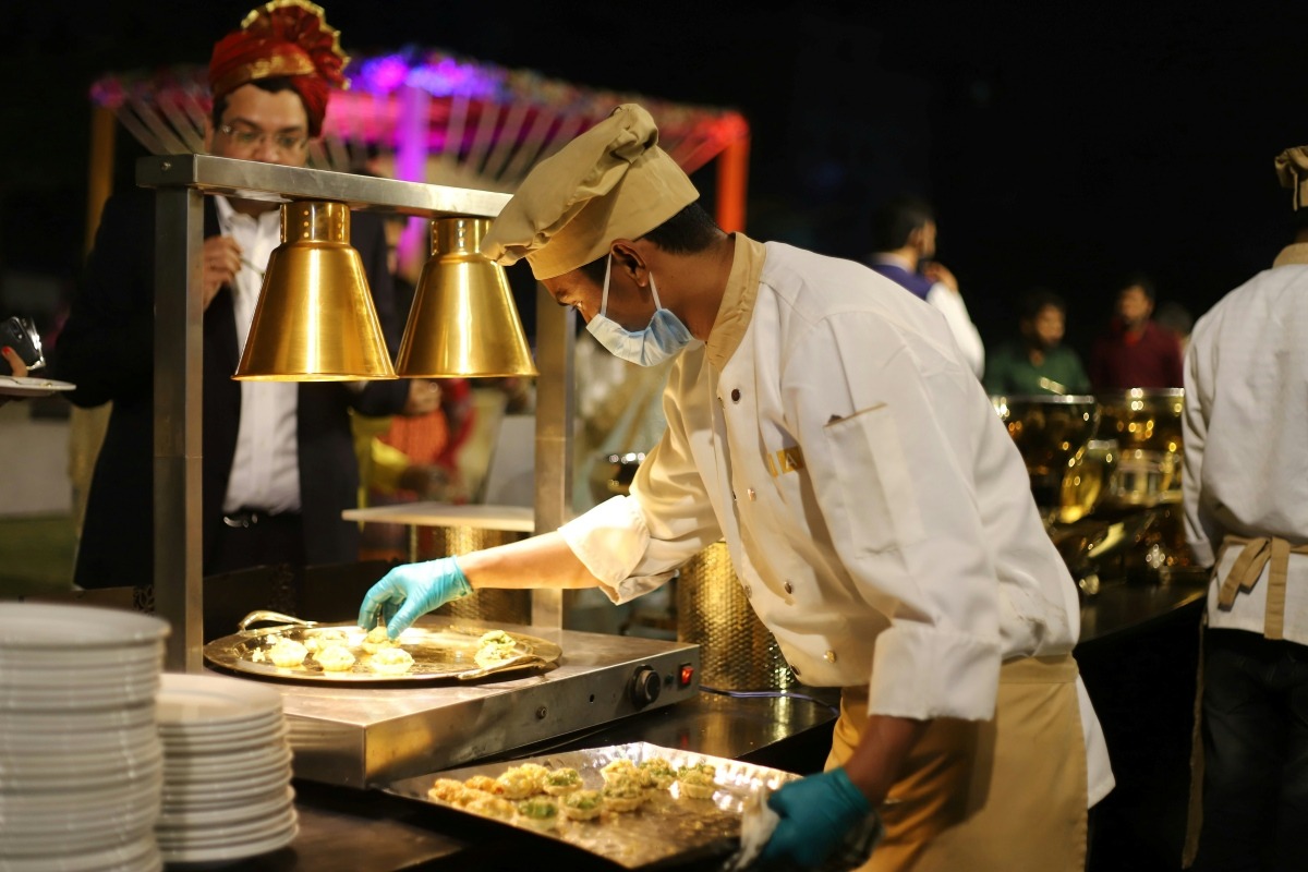Chef plating hors d'oeuvres under heat lamps at an evening event, the kind of high-volume service catering management software helps coordinate behind the scenes.