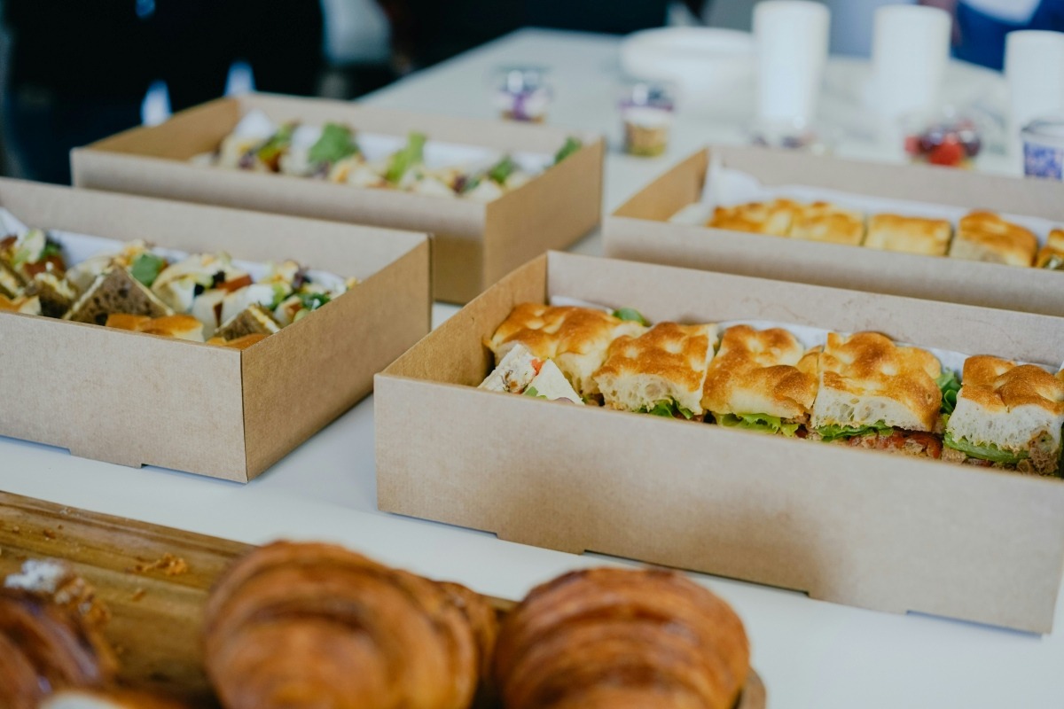 Boxed sandwiches, wraps, and pastries laid out for a catered lunch or grab-and-go order.