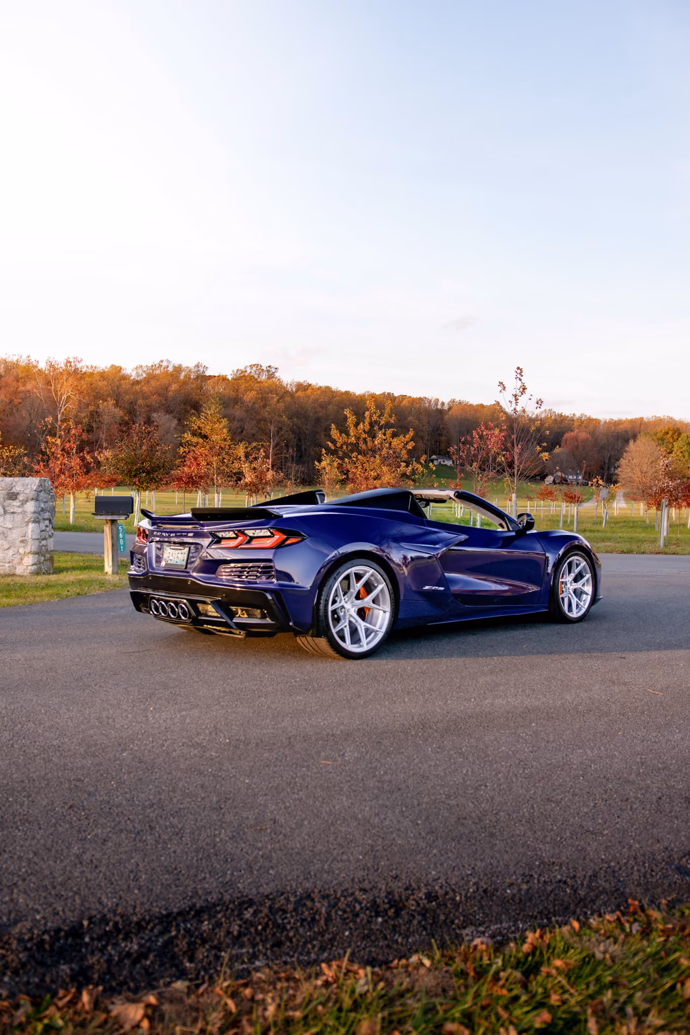 Purple Corvette C8 with Forgelite FL1 aftermarket wheels parked on a paved road with fall-colored trees and green fields in the background during a clear day.